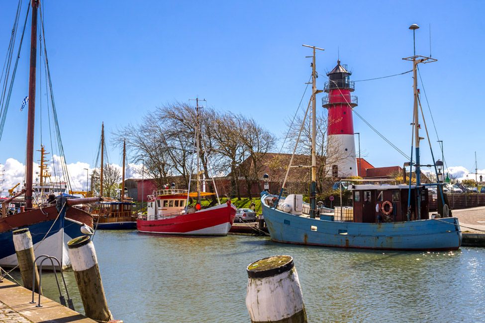 Farbenfrohe alte Kutter im Büsumer Hafen mit einem rot-weißen Leuchtturm im Hintergrund